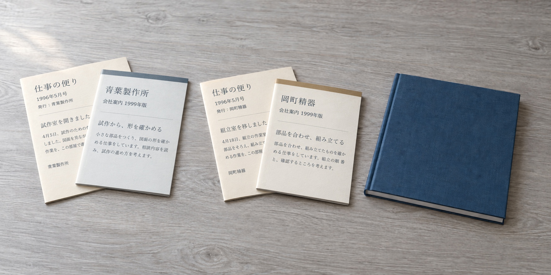 二社それぞれの社内報・会社案内と、一冊の青い冊子を机に並べた様子。