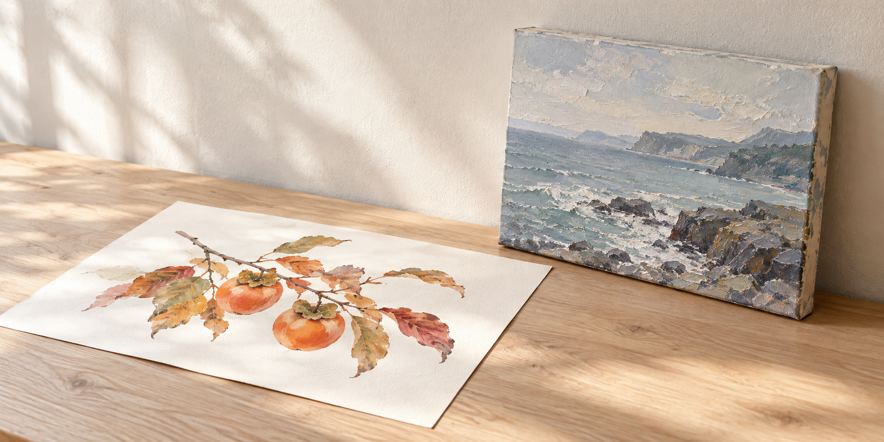机に置いた柿の水彩画と、絵具の凹凸や側面の厚みが見える海辺のキャンバス画。