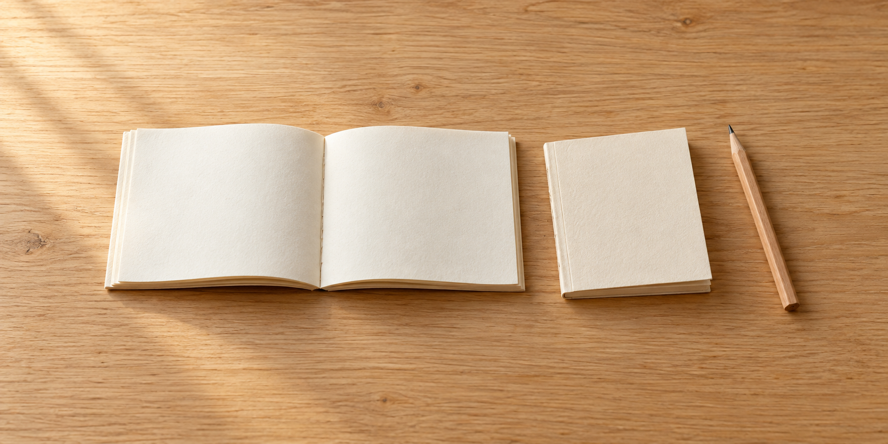 開いた白い小冊子と、閉じた冊子、一本の鉛筆を木の机に並べている。