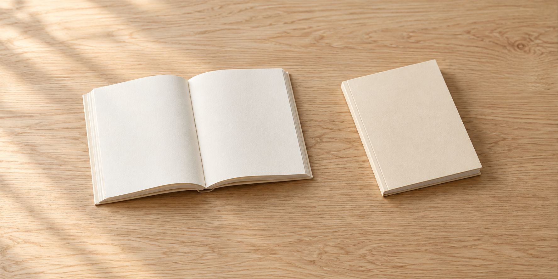 無地の本の見開きと閉じた冊子を、木の机に間隔を空けて置いている。